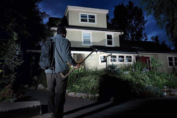 A photograph of a burglar approaching a home at night.