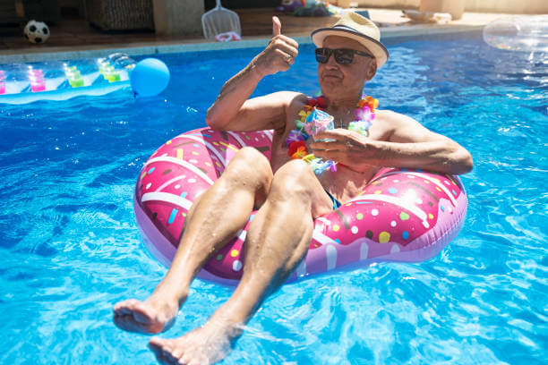 Senior man relaxing in floating ring in the swimming pool. He is drinking juice cocktails.