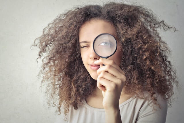 Portrait Photo of Woman Holding Up a Magnifying Glass Over Her Eye