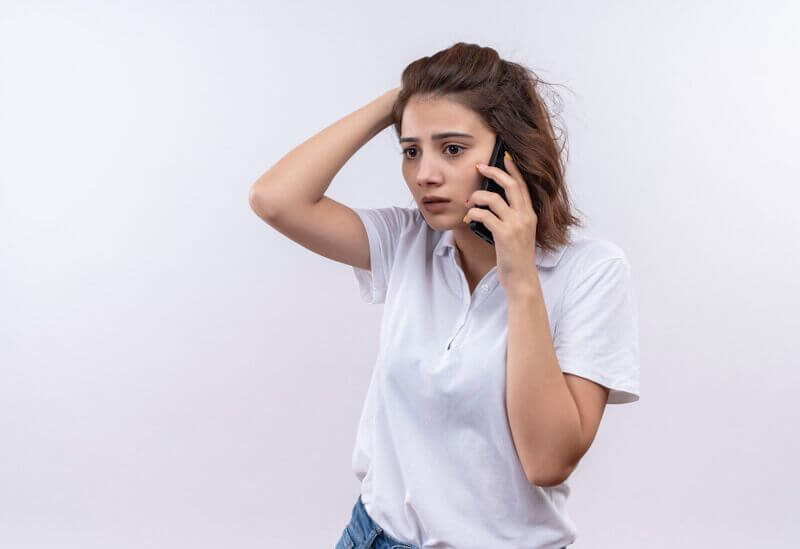 Young girl with short hair wearing white polo shirt looking confused and very anxious while talking on mobile phone
