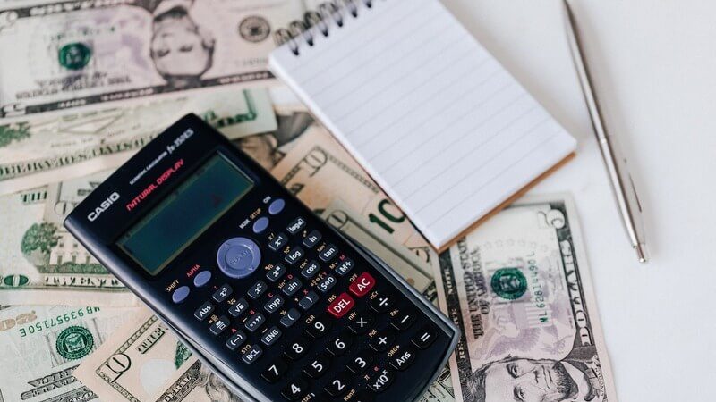 Calculator and notepad placed on USA dollars stack
